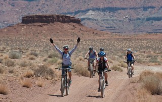 Group riding bicycles through the desert. Rider with hands upraised in joy.