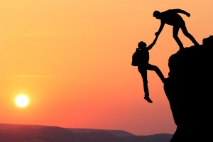 Mountain climber helping another scale a cliff