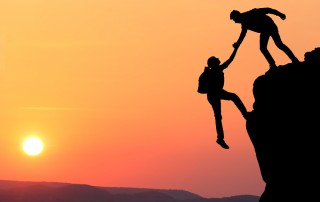 Mountain climber helping another scale a cliff