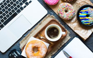 Image of laptop computer and cup of coffee at work surrounded by doughnuts