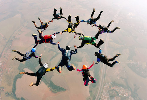 Image of a group of parachutists coming together to join hands in the air.